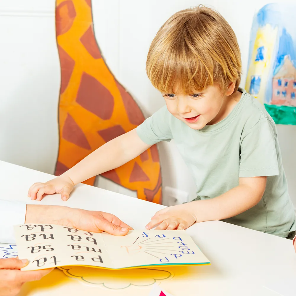 A child smiling and looking at a school book at a Little Newtons daycare
