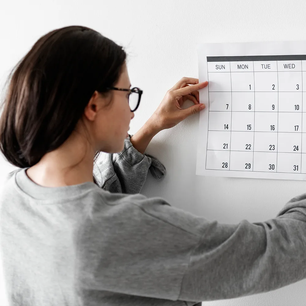 An adult looking at a calendar held up to a wall.