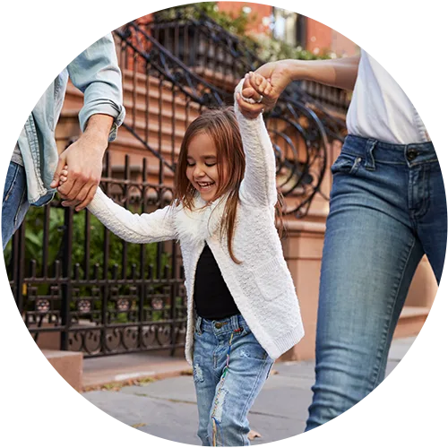 A child holding hands with two adults, smiling and walking down a street