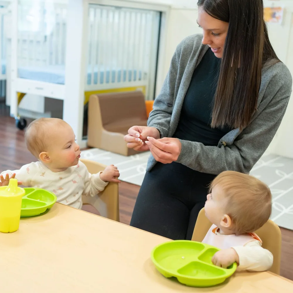 A teacher feeding two small toddlers at a table at a Little Newtons daycare