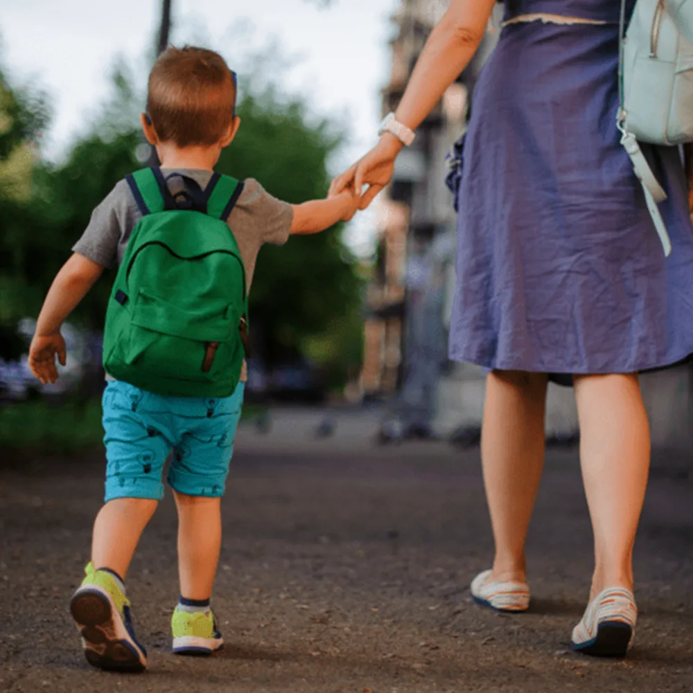 A child with a green backpack holding his mother's hand walking