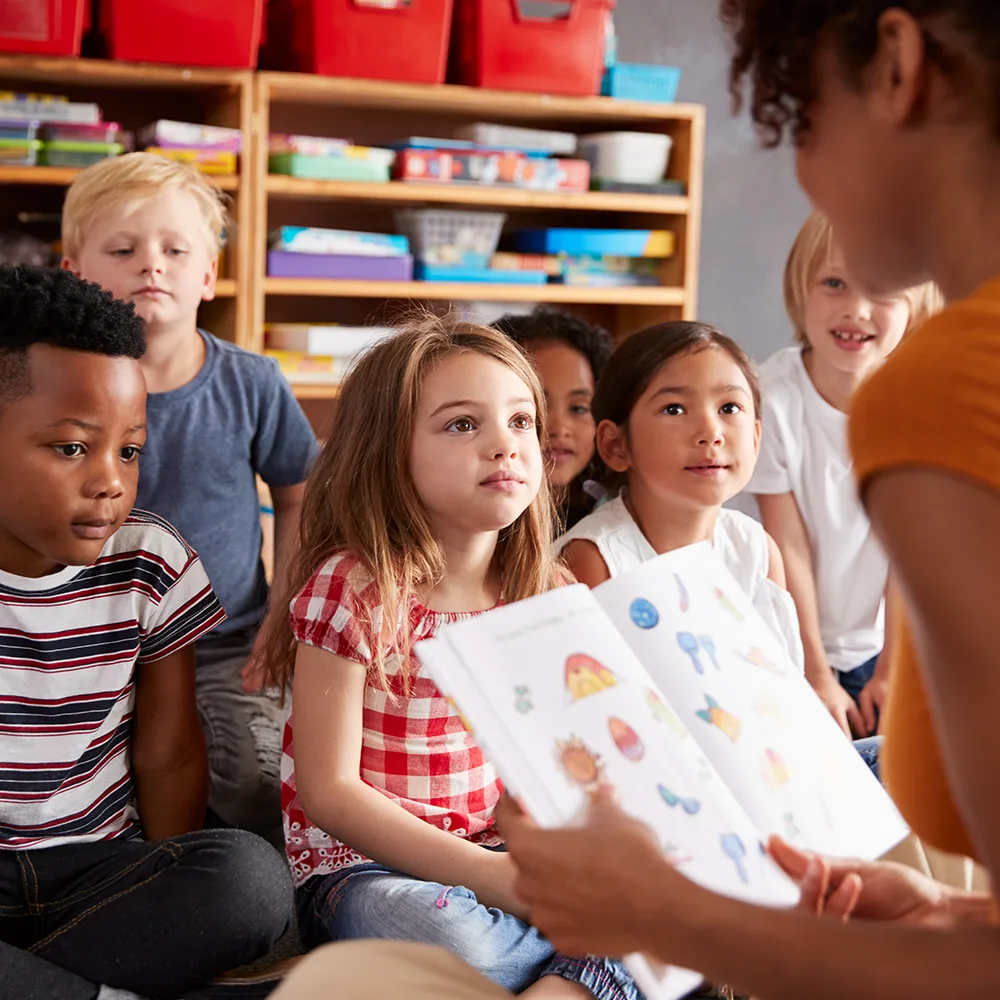 Children listening to a teacher read from a picture book at a Little Newtons daycare