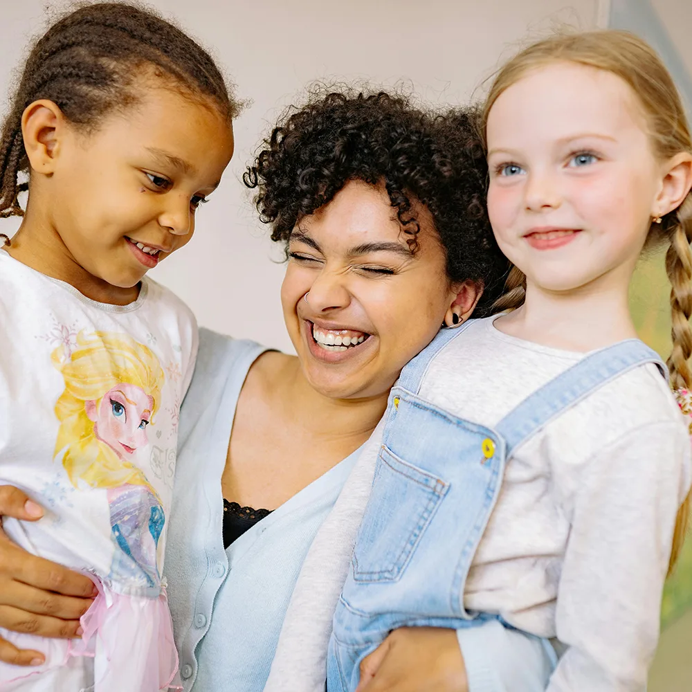 An adult hugging two children and smiling at a Little Newtons daycare