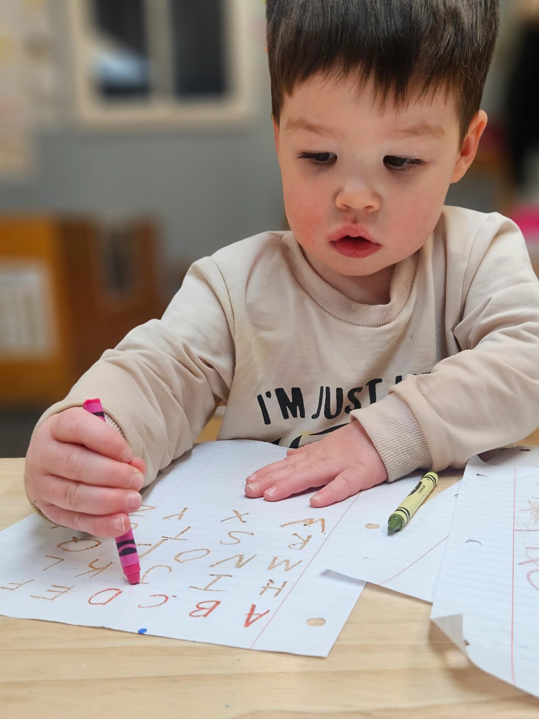 Child coloring the alphabet at a table at Little Newtons daycare.