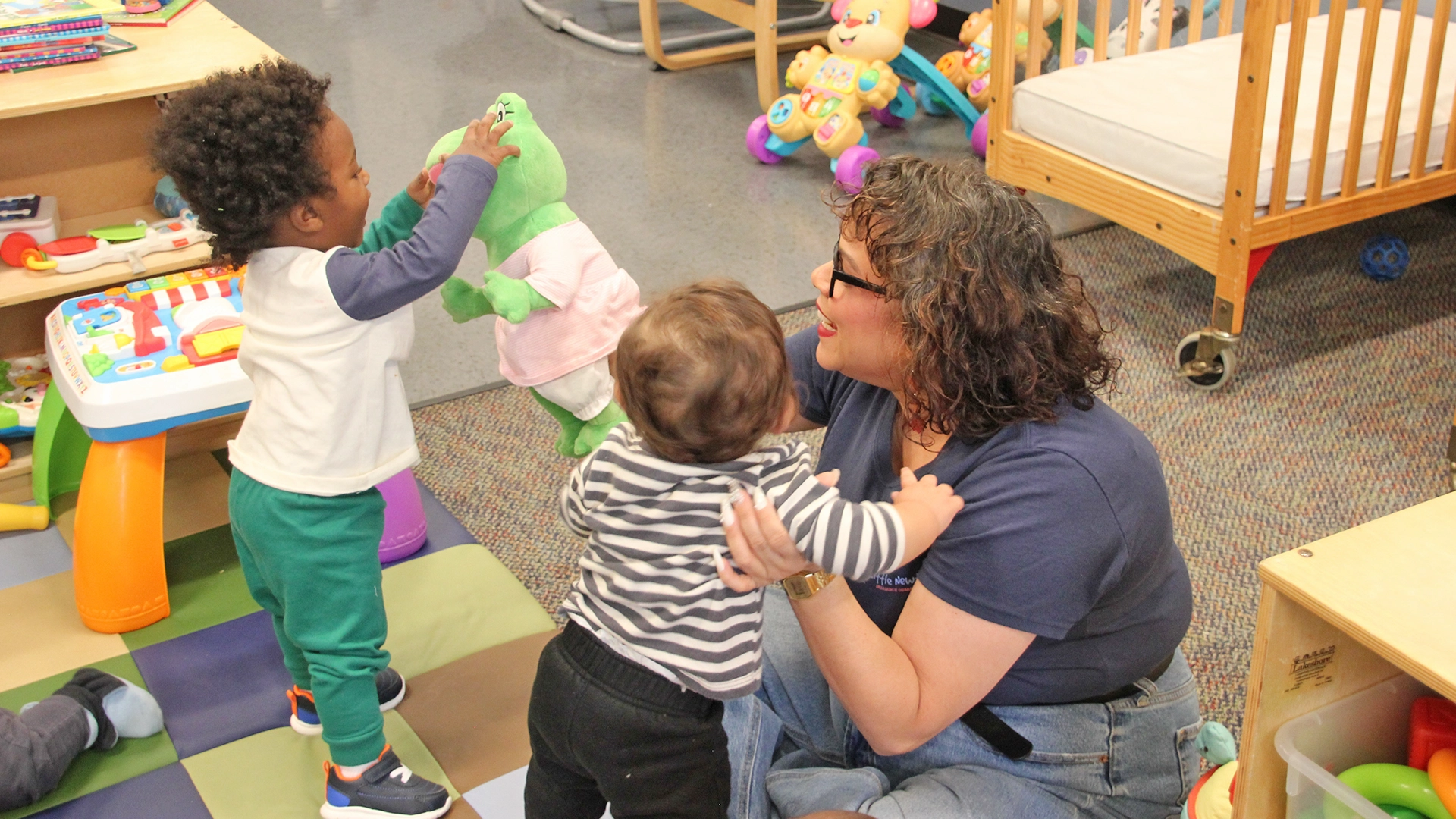 A teacher playing with toddlers on the floor of a Little Newtons