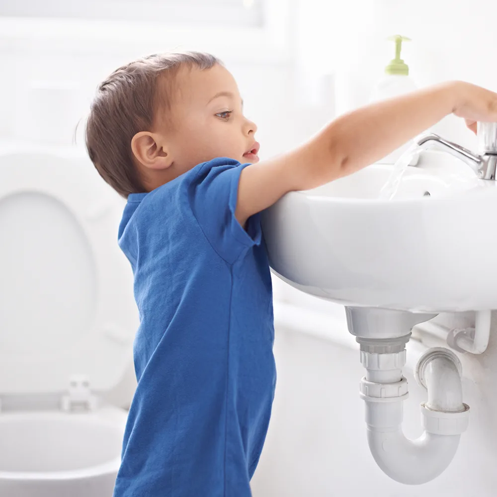 A child reaching up to use a sink