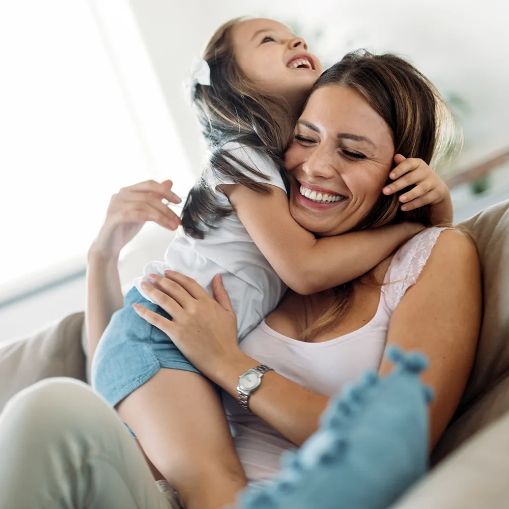 A mother smiling and holding a child on a couch