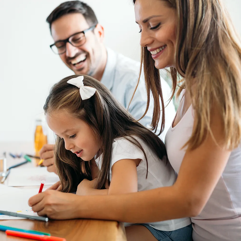 A laughing mother and father helping their child write in a book at a Little Newtons daycare