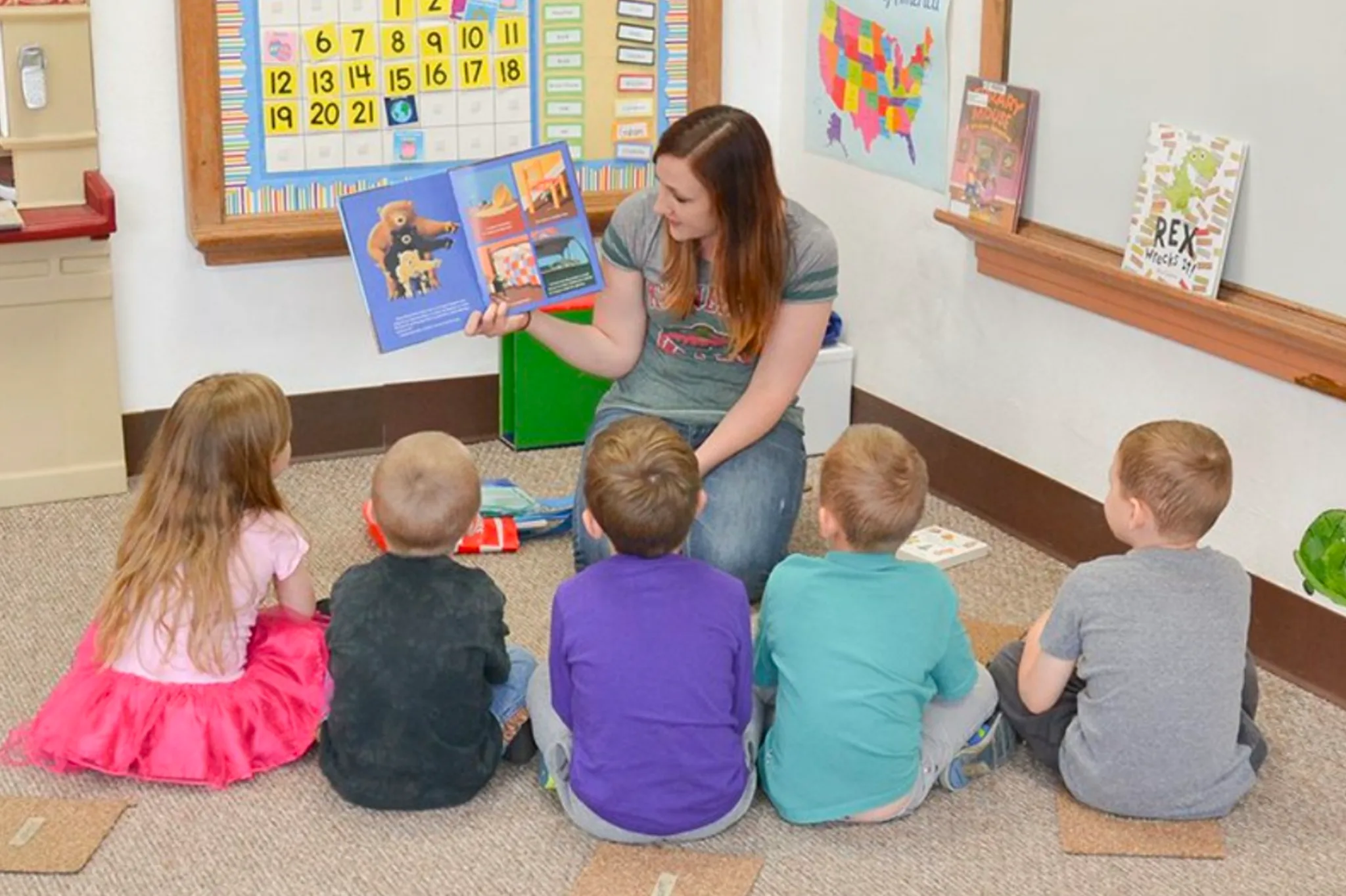 Kids sitting down listening to a teacher read a book