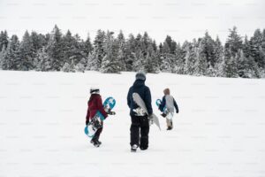 2 children and a parent walking through snow with snowboards